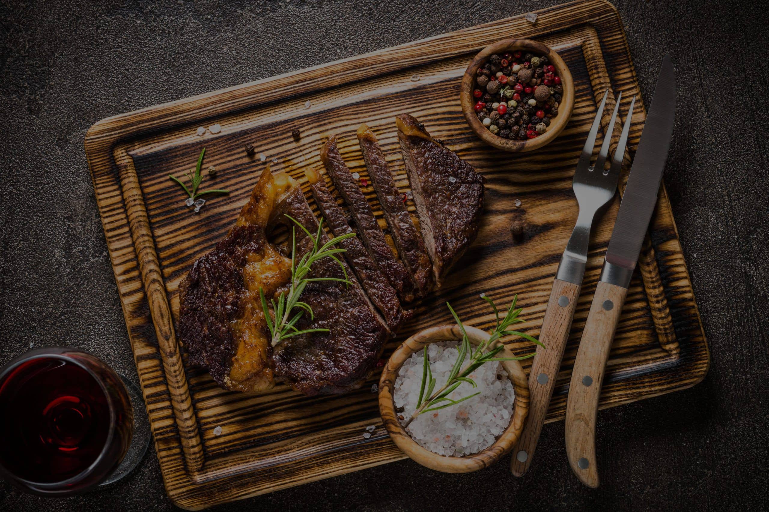 Grilled beef on a wooden carving board with rosemary and peppercorns